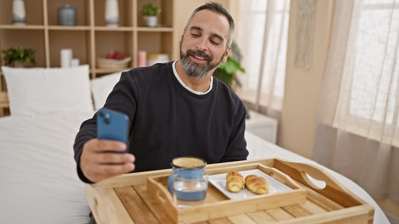 成熟的大胡子男人在床上享用早餐，在光线充足的卧室里自拍视频素材