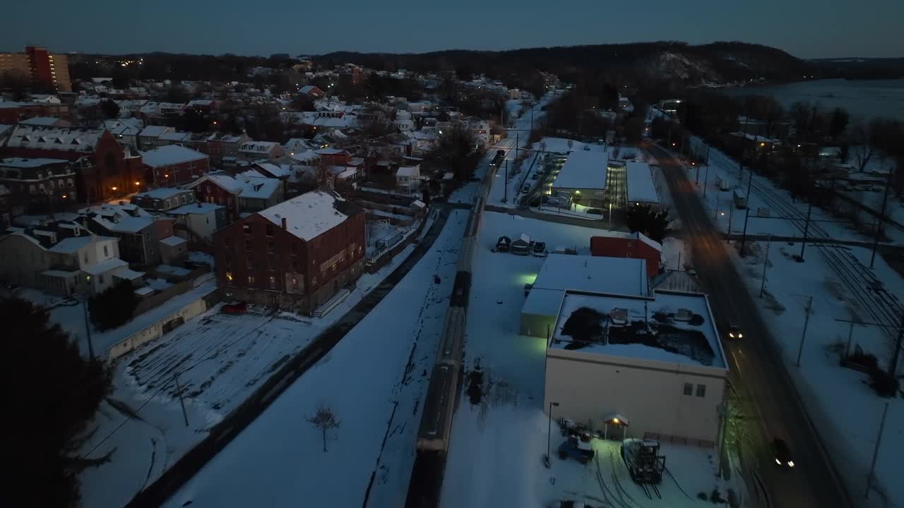 航拍鸟瞰火车在美国小镇的雪道上的夜晚。冬季场景中建筑物和灯笼的照明。美国一个小镇的郊区。无人机的立交桥。视频素材