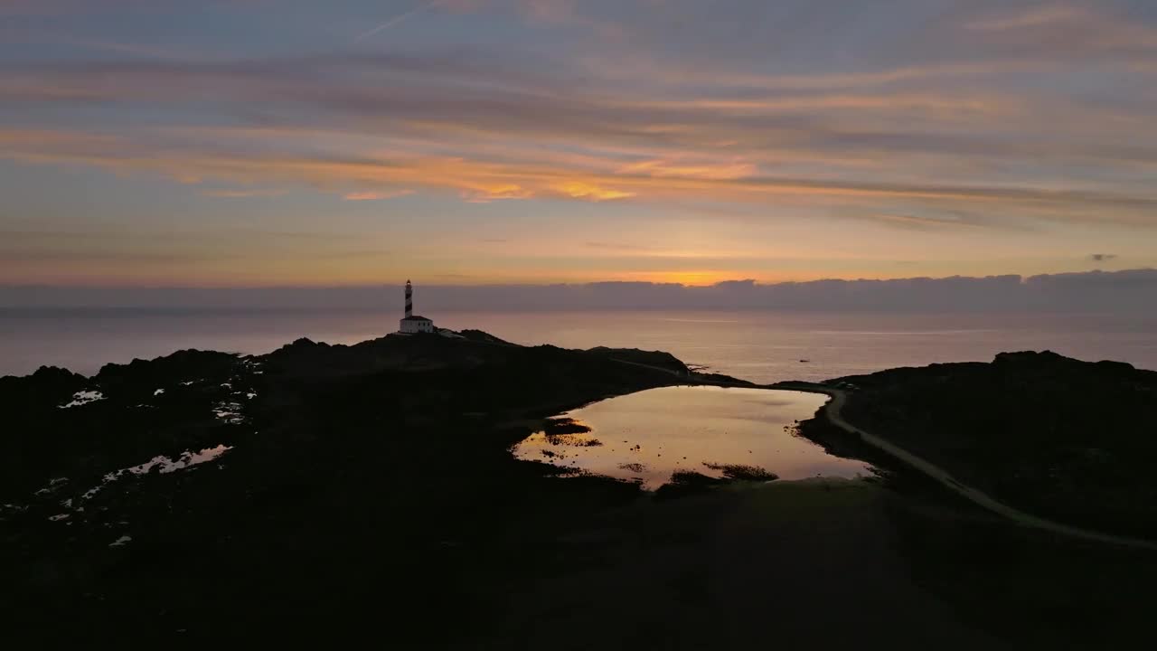 无人机日落景观梅诺卡海岸灯塔海滩海岸在梯度海水，黄金小时彩色天际线视频素材