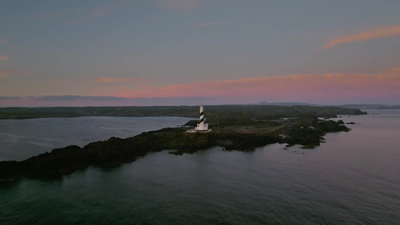 空中灯塔悬崖在粉红色的日落天际线梅诺卡海水景观西班牙沿海旅游目的地，无人机拍摄视频素材