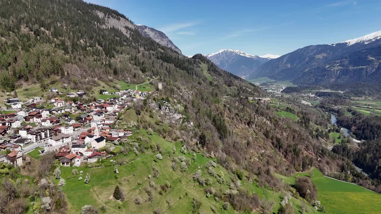 美丽的瑞士小镇在绿色的山坡上。瑞士的Trin镇。以雪峰为背景的山脉。春天的蓝天和阳光。无人机前镜头。视频素材