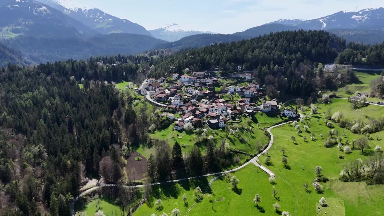 阳光下瑞士绿山上田园诗般的小镇。背景是阿尔卑斯山的雪山。空中前进。视频素材