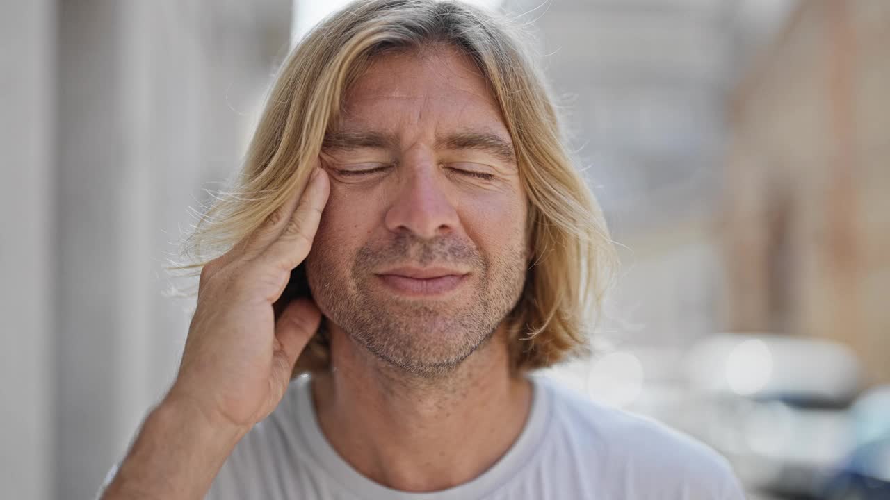 一个痛苦的长着金色头发的男人在城市的街道上举着他的头。视频素材