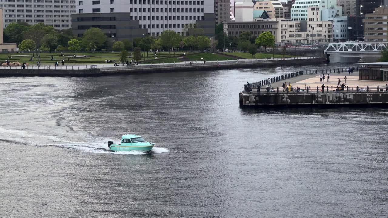 蓝绿色的水上出租车在河上疾驰，背景是城市景观和停靠的人，阴天视频素材