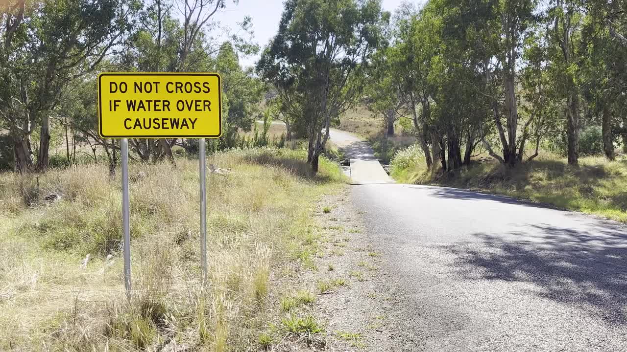 在新南威尔士州地区的一条堤道前，一条干燥而尘土飞扬的道路上立着一个洪水警告标志视频素材