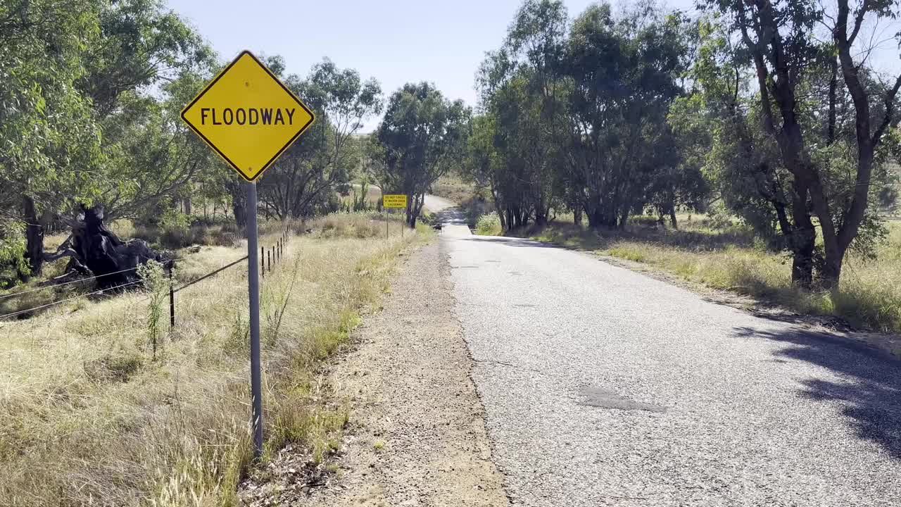 在新南威尔士州地区的一条堤道前，一条干燥而尘土飞扬的道路上立着一个洪水警告标志视频素材