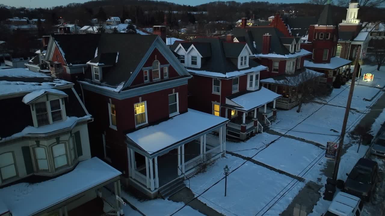 在下雪的冬日里，单户住宅窗户上温暖的灯光。美国城市里被雪覆盖的屋顶和门廊。天线自上而下上升。视频素材