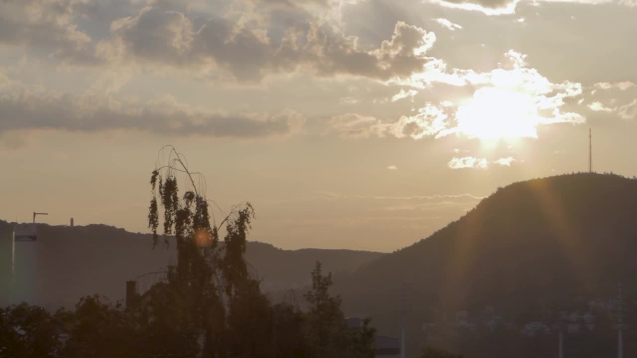 黄金时刻的太阳穿透云层，在丘陵景观的剪影上，宁静的天空为背景视频素材