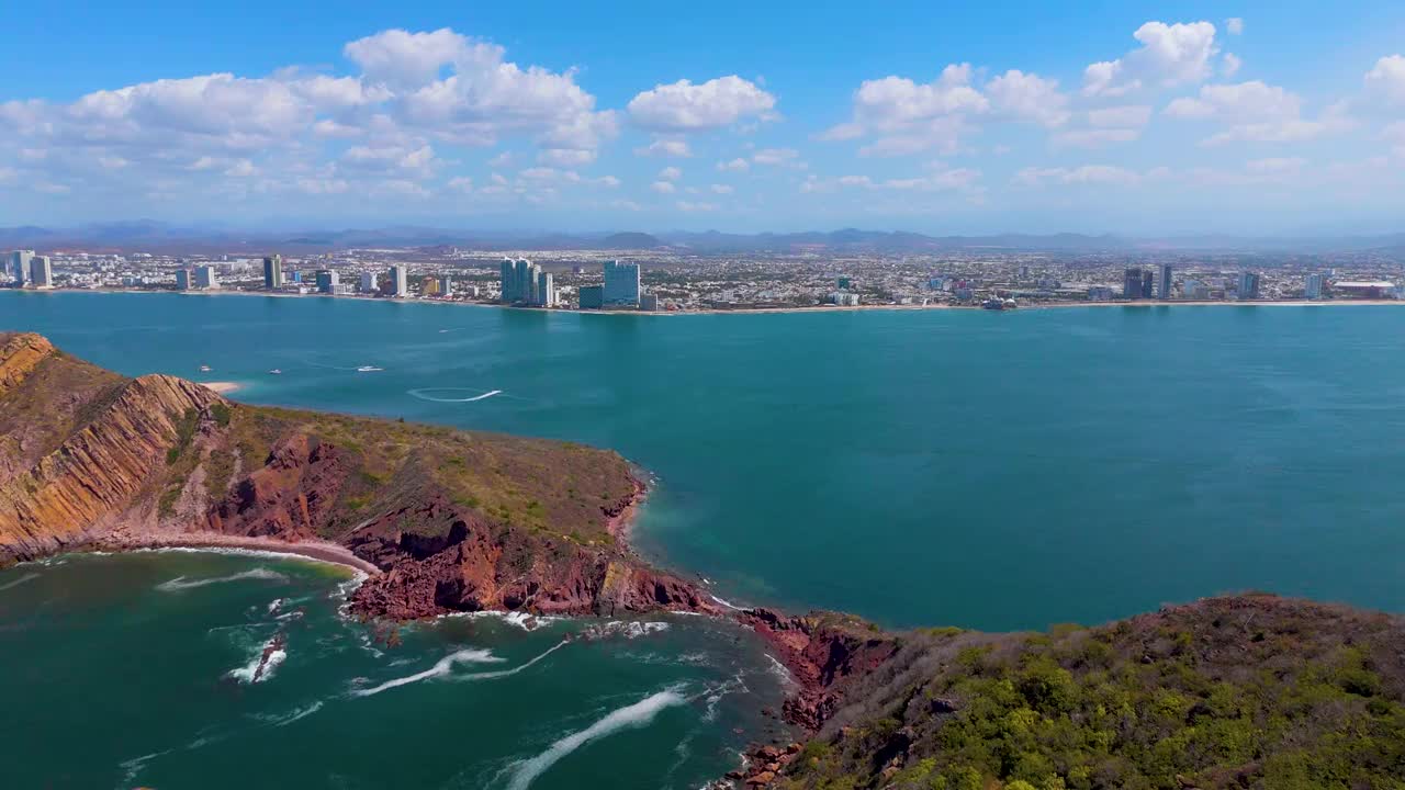 从荒岛到墨西哥马萨特兰海滩的惊险空中之旅。游船在蓝色的海面上留下白色的尾迹，增强了壮观的景色。当无人机靠近海滩时，突出的酒店增加了这个墨西哥人的宏伟视频素材