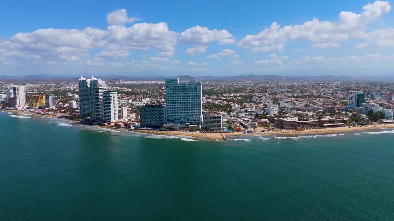 从荒岛到墨西哥马萨特兰海滩的惊险空中之旅。游船在蓝色的海面上留下白色的尾迹，增强了壮观的景色。当无人机靠近海滩时，突出的酒店增加了这个墨西哥人的宏伟视频素材