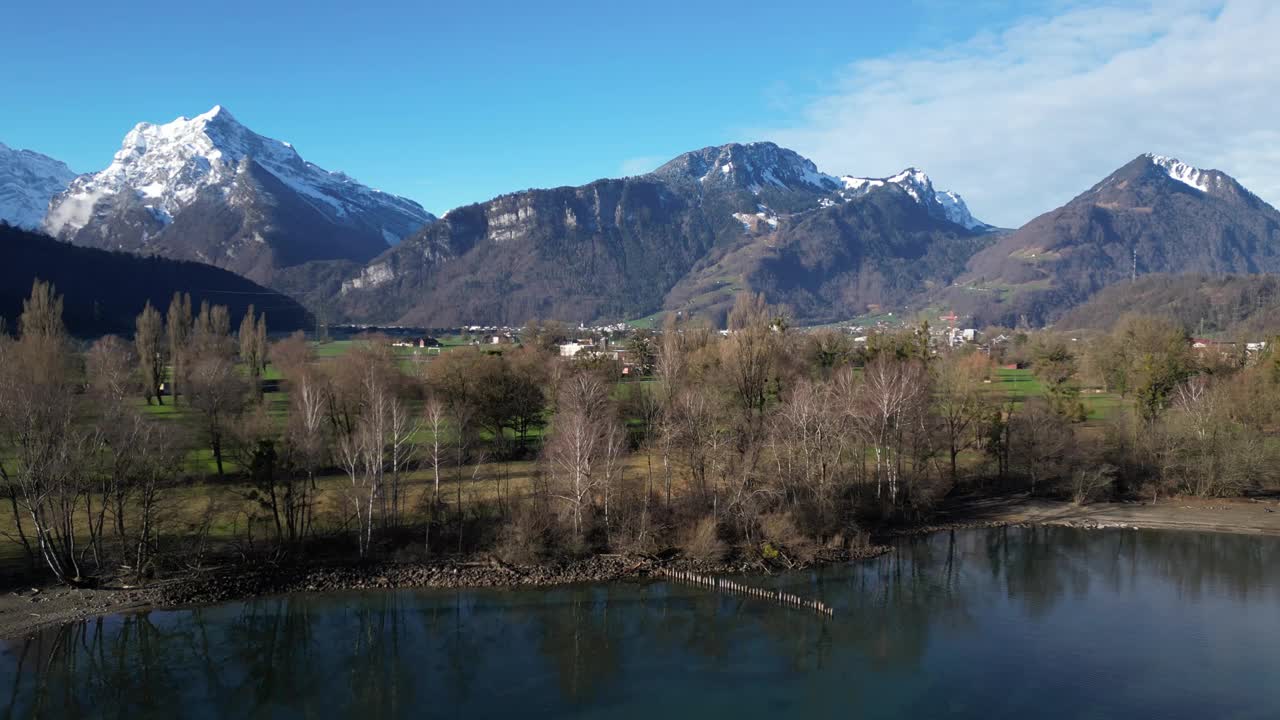 平移无人机剪辑显示瑞士阿尔卑斯山的雪山，前景是草地低地和湖岸视频素材