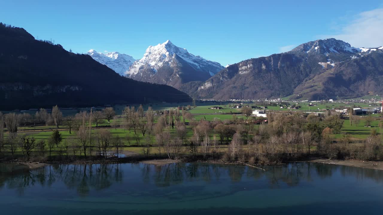 无人机剪辑显示雄伟的雪山与郁郁葱葱的绿色土地和湖泊的前景视频素材