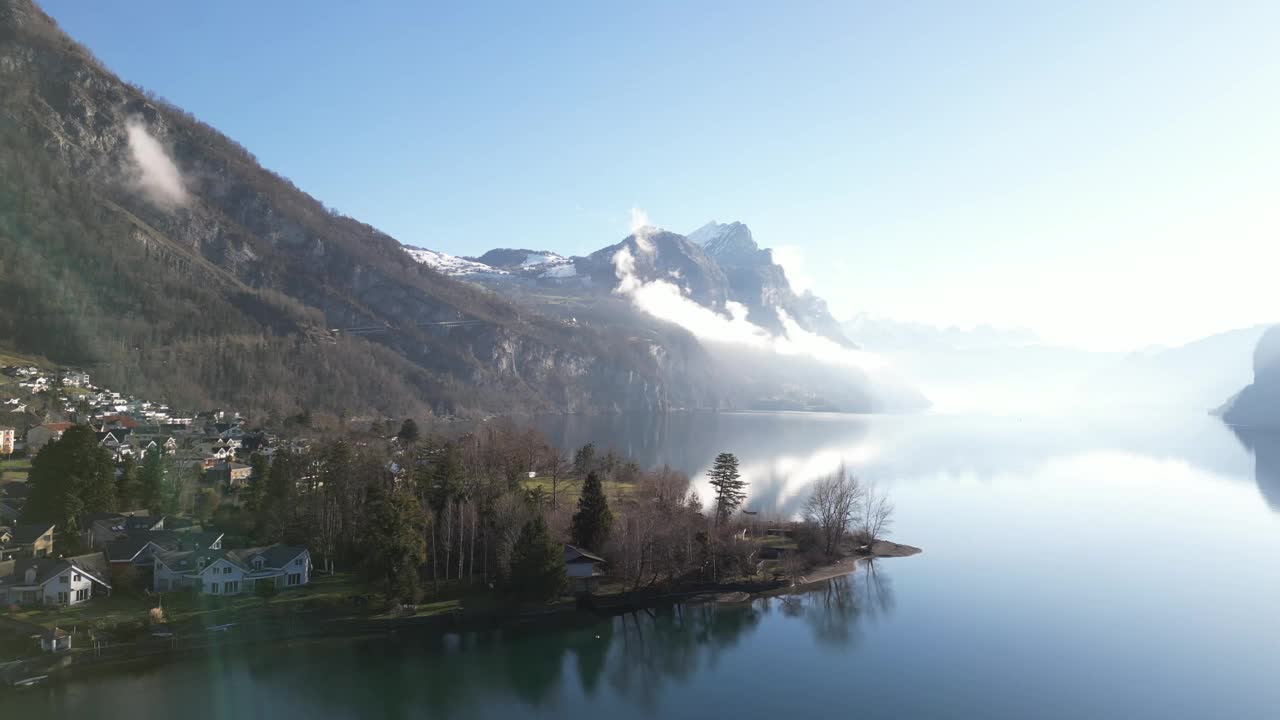 明亮的无人机剪辑与镜头光晕显示雾蒙蒙的雪山旁边的平静的湖在瑞士视频素材