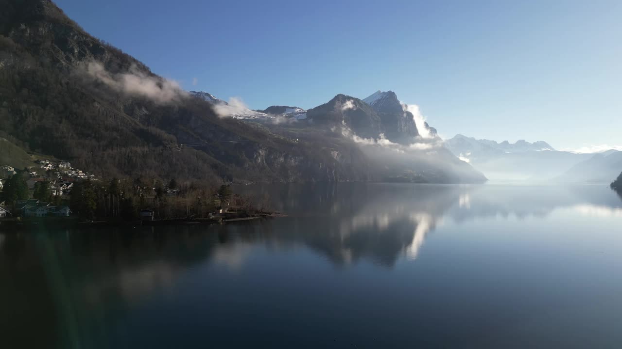 无人机剪辑显示湖泊海岸线与薄雾和雪山在明亮的晴天视频素材