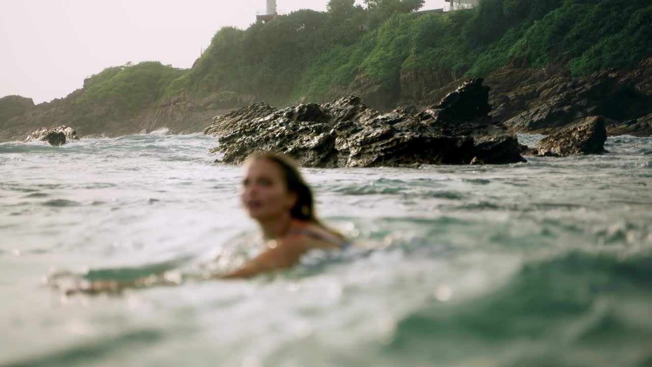 优雅的女人沐浴在海洋，嬉戏的海浪拥抱她在浪漫的海滩设置。穿着飘逸的服装，女士享受宁静的水，放松的氛围，在黄金时间自然海岸线的背景。Slowmo视频素材