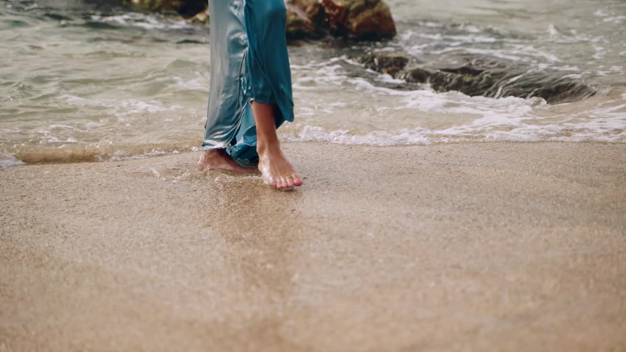 赤脚的女人穿着飘逸的裙子走出大海，来到沙滩上，海浪拍打着脚，自由，放松的本质，夏天的共鸣。完美的浪漫度假主题，时尚的生活方式，宁静的假期。Slomo视频素材