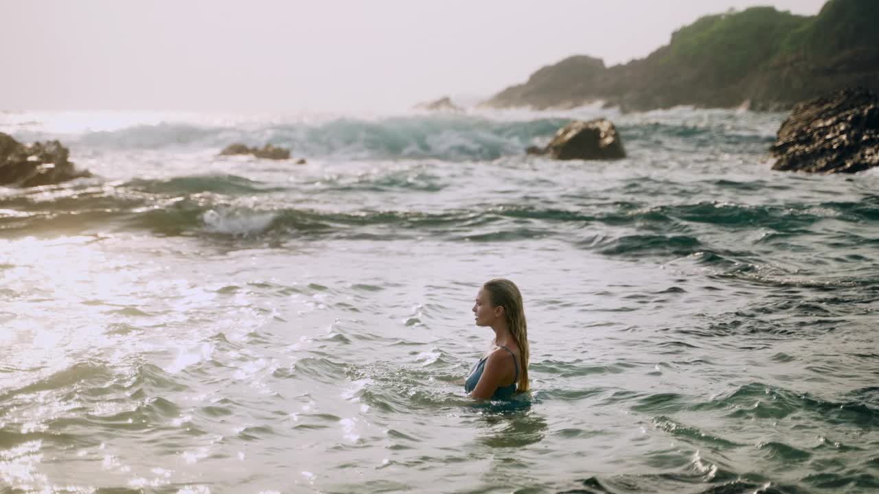 优雅的女人在美丽的海滩享受日落时的海浪。优雅的女性沐浴在大海中，宁静的夏日氛围。美景、自然相约于宁静的海滨风光，生活方式瞬间旅行。视频素材