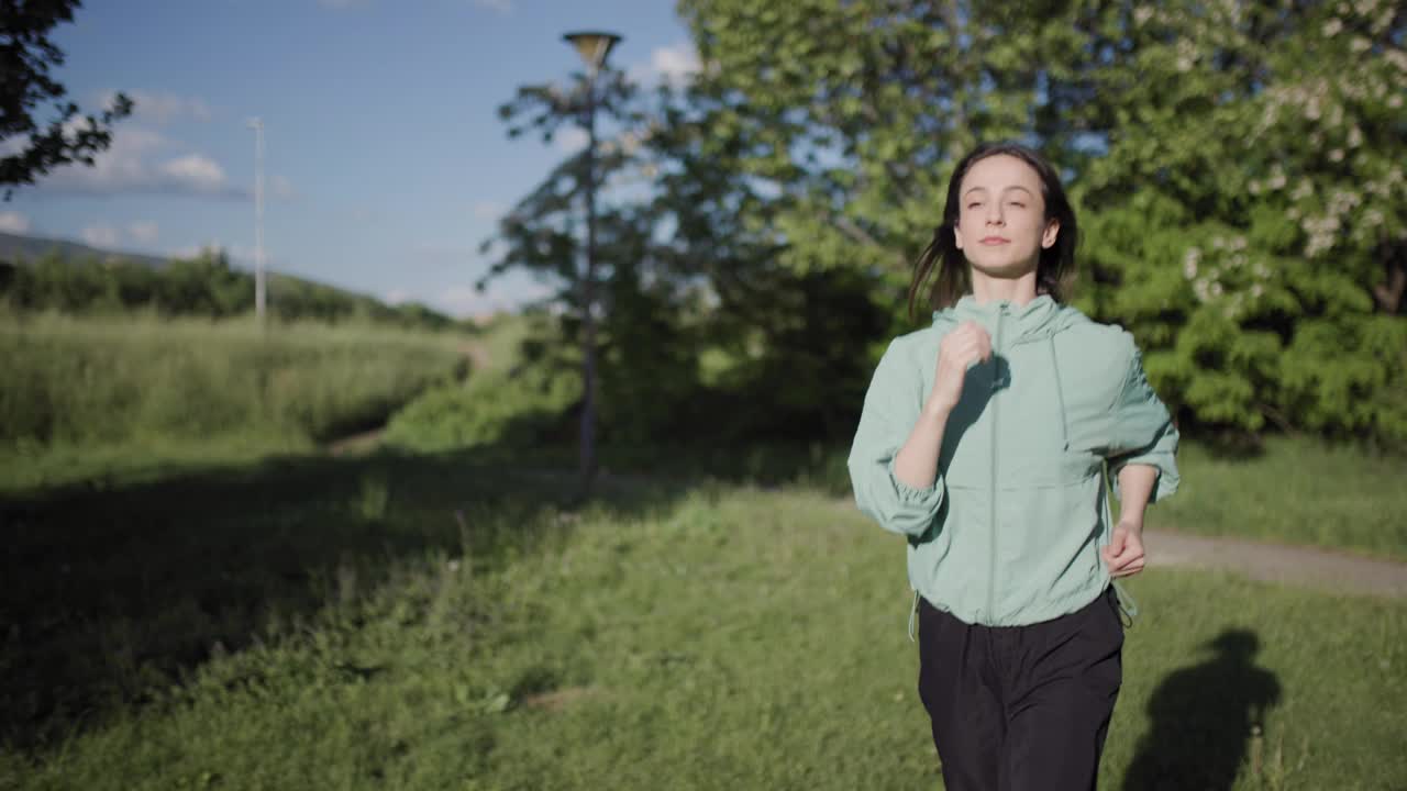 这张照片拍摄于一个宁静的公园，一位年轻女子穿着休闲运动服舒适地慢跑，体现了大自然中的活力和积极的生活方式。视频素材