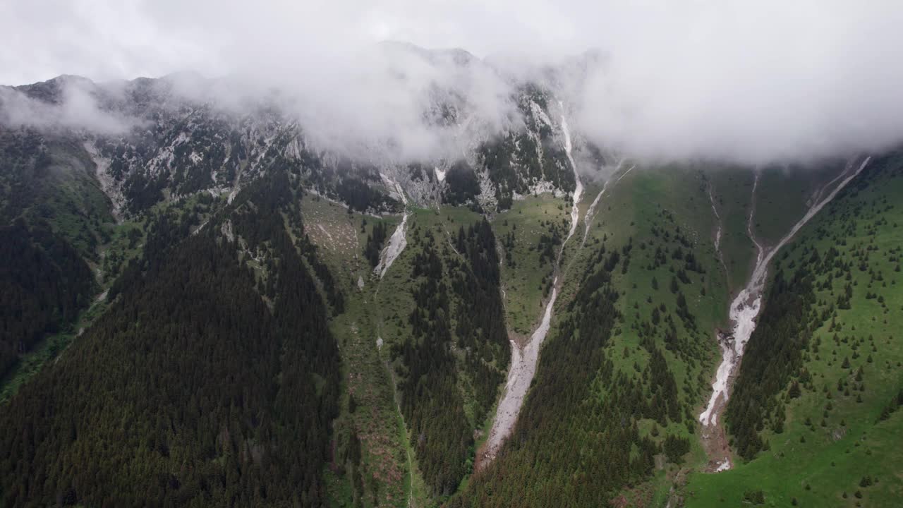 雾蒙蒙的山峰上有雪，下面是葱郁的绿色山谷，鸟瞰视频素材