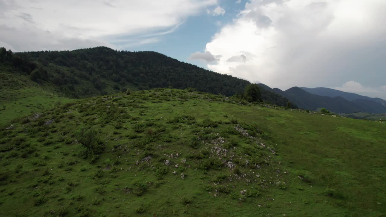 郁郁葱葱的山丘附近有一个村庄，多云的天空下，宁静而广阔的景观，鸟瞰视频素材