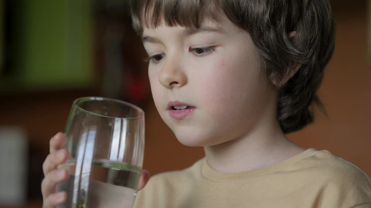 男孩从杯子里喝干净的水。小男孩在家里喝玻璃新鲜透明纯过滤矿泉水。特写孩子喝杯水健康的身体护理。健康的生活方式。视频素材