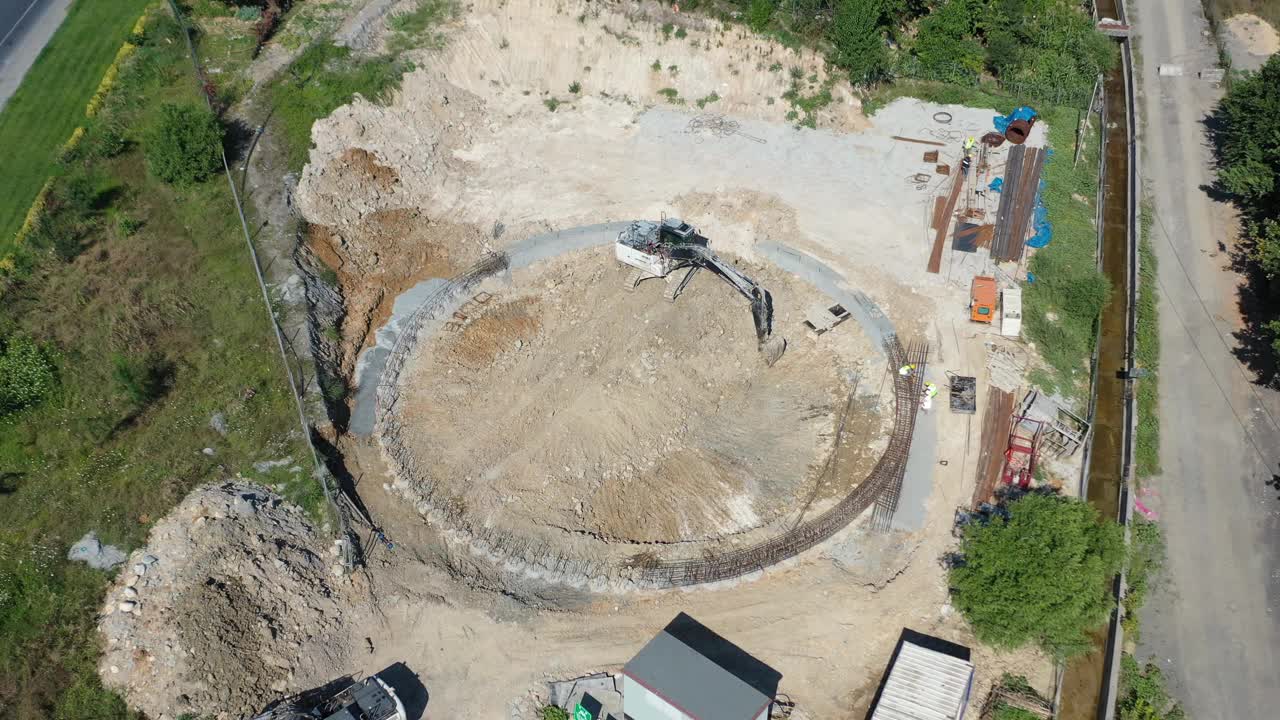 鸟瞰图，一台挖掘机正在挖掘一个大型圆形建筑工地视频下载