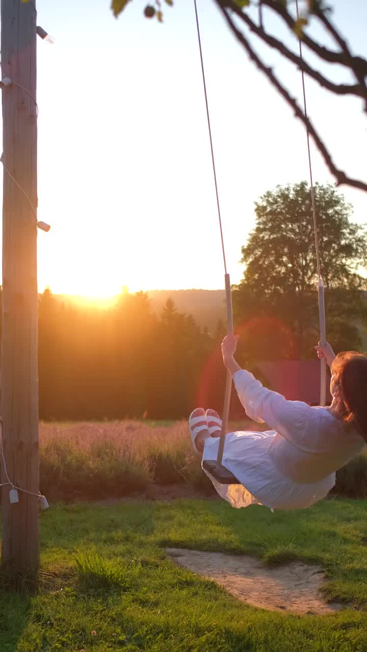 穿着白裙子的漂亮女人在夕阳下的薰衣草田前荡秋千视频素材