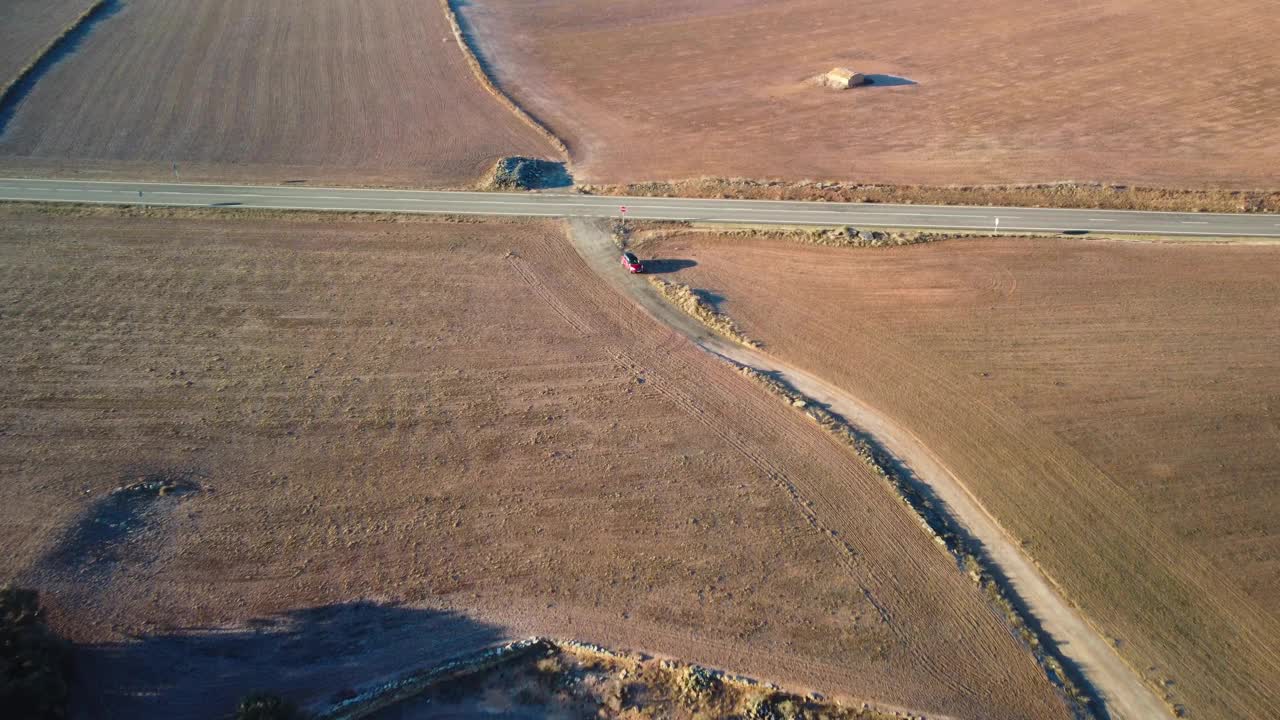 一辆汽车在乡村公路上行驶，穿过加泰罗尼亚莱伊达的田野，干燥的风景和蜿蜒的小路，鸟瞰视频素材