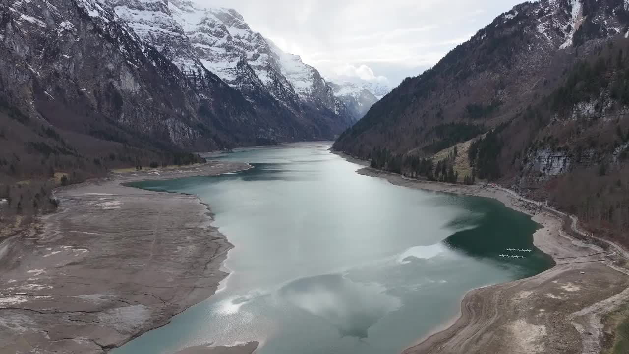 鸟瞰图Klöntalersee与湖反映周围的雪山和可见的淤泥沉积视频素材