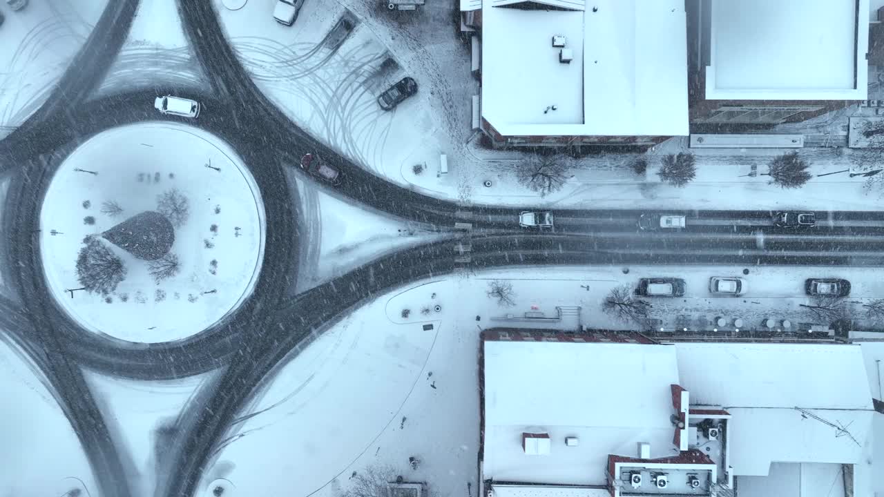 白雪覆盖的城镇广场，环岛和雪花飘落。在暴风雪条件下，空中俯瞰的卡车拍摄交通。古雅小镇的圣诞装饰。视频素材