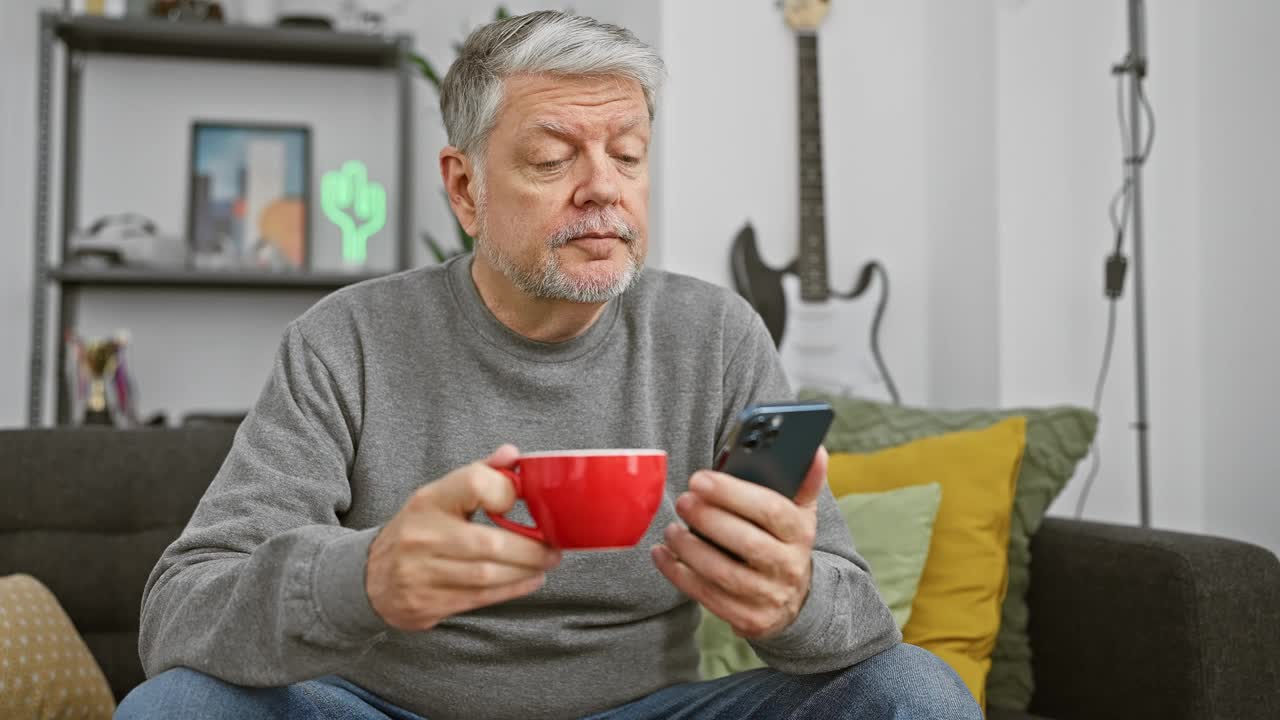 一个白发苍苍的成熟男人在客厅里喝着咖啡，玩着智能手机。视频素材