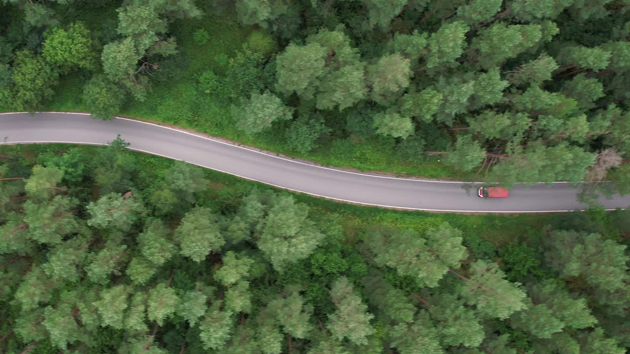鸟瞰图夏日，红色汽车行驶在柏油路上，穿过广阔的森林。汽车在松林道路上行驶的航拍照片。穿越森林的公路旅行。风景优美的夏季景观。视频素材