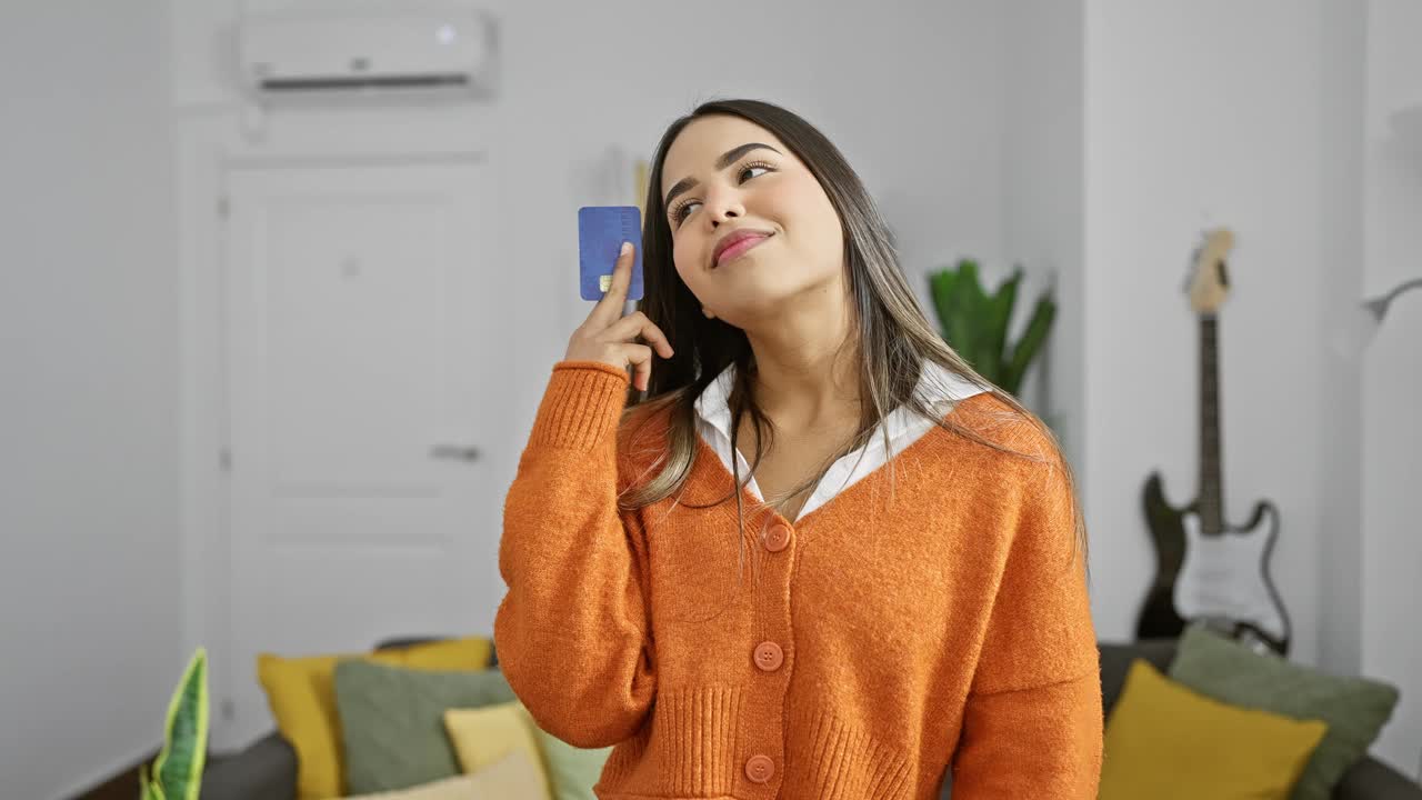 一位深思熟虑的西班牙裔妇女在室内拿着信用卡，在舒适的客厅里考虑购买。视频素材