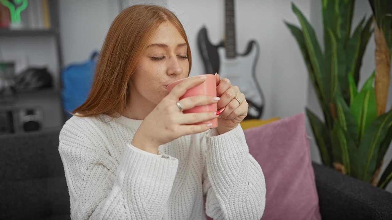 一位沉思的年轻女子在舒适的客厅里享受着一杯热饮，增添了一种宁静、家常的氛围。视频素材