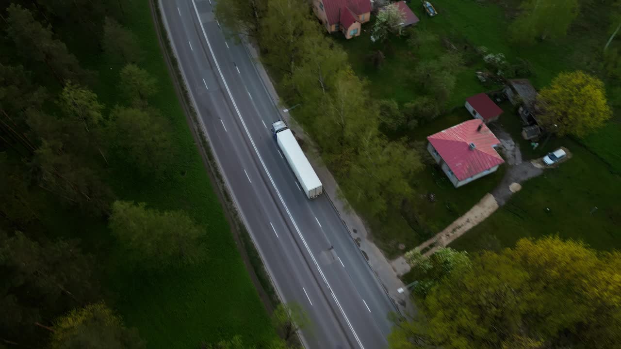 鸟瞰图，一辆卡车行驶在乡村道路上，经过房屋和树木，展现了一个绿色的乡村景观视频素材