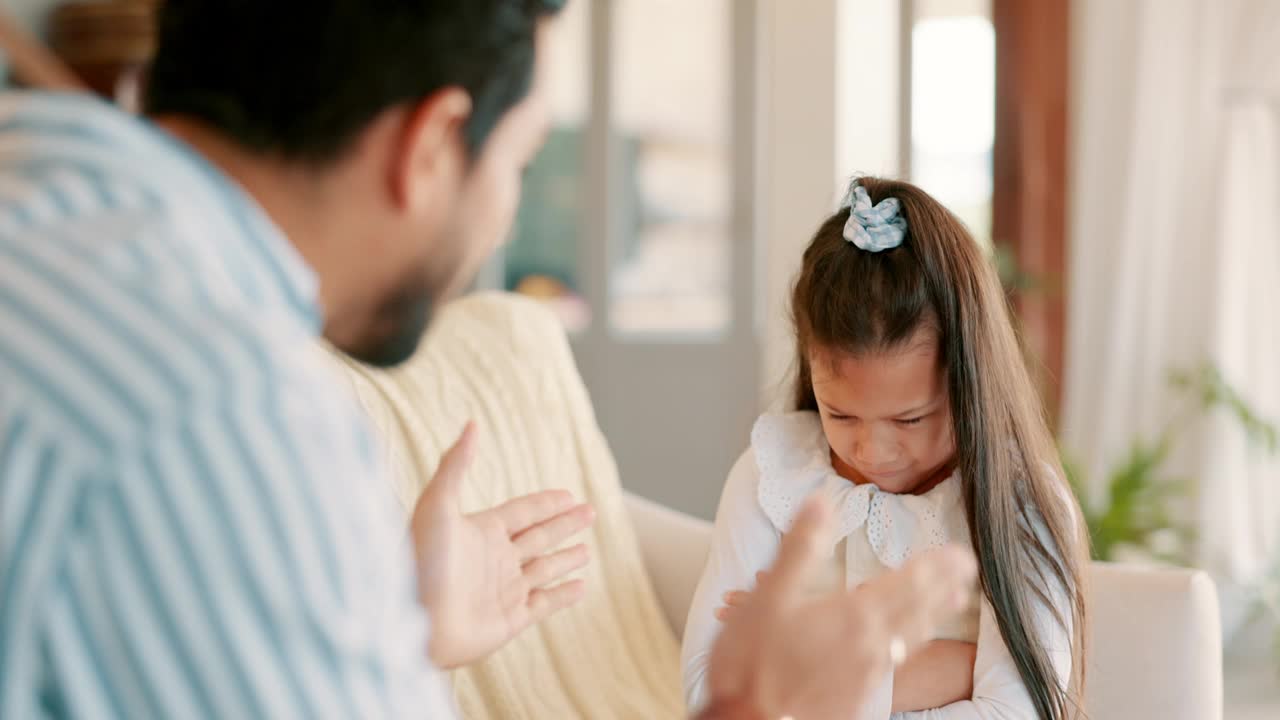 因为冲突，父亲和他的女儿在家里的客厅里受到惩罚。生气，喜怒无常，年轻的父亲大声说话或责骂他的孩子在家里的沙发上的不良行为。视频素材