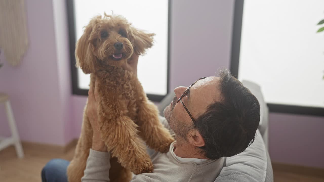 一位中年男子和他的贵宾犬在舒适的客厅里享受着美好的时光，描绘了主人和宠物之间的纽带。视频素材