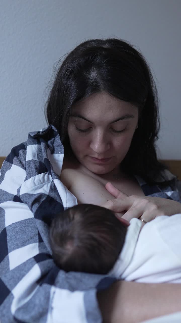 母亲给新生婴儿喂奶，捕捉一个温柔而亲密的时刻，营养和联系。母亲的凝视表明了她对孩子的爱和联系视频素材