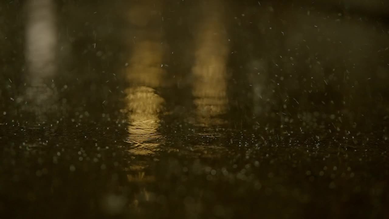 夜晚，雨点落在潮湿的地面上，反射光线，在城市街道上营造出黑暗的气氛视频素材