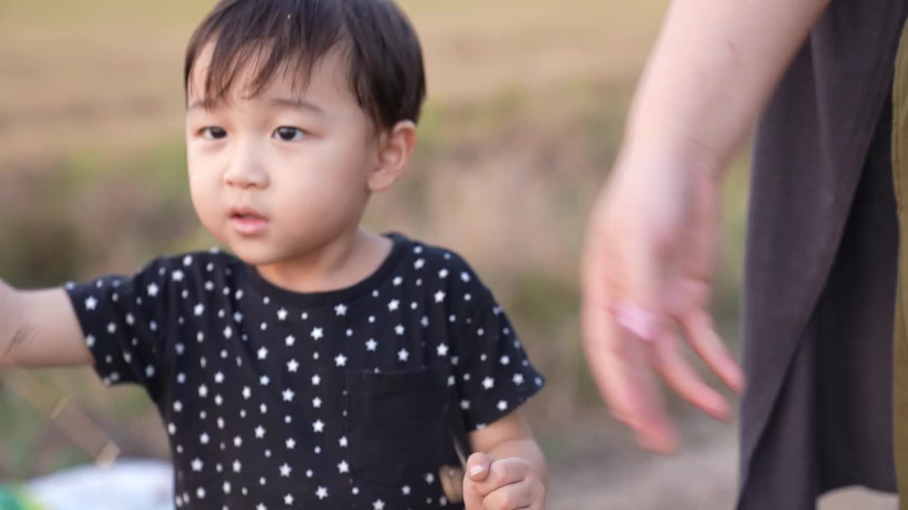 亚洲可爱男孩和妈妈在田野里玩花。全家在公园度假。课堂外教育概念。视频下载