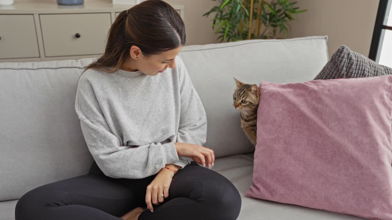 在舒适的客厅里，一位年轻的西班牙妇女和她的宠物猫坐在沙发上，装饰现代，室内气氛轻松。视频素材