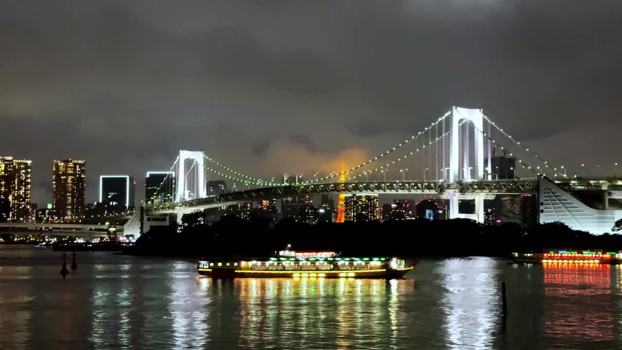 夜晚，五颜六色的船只在灯火通明的大桥下巡游，映衬着城市的天际线视频素材