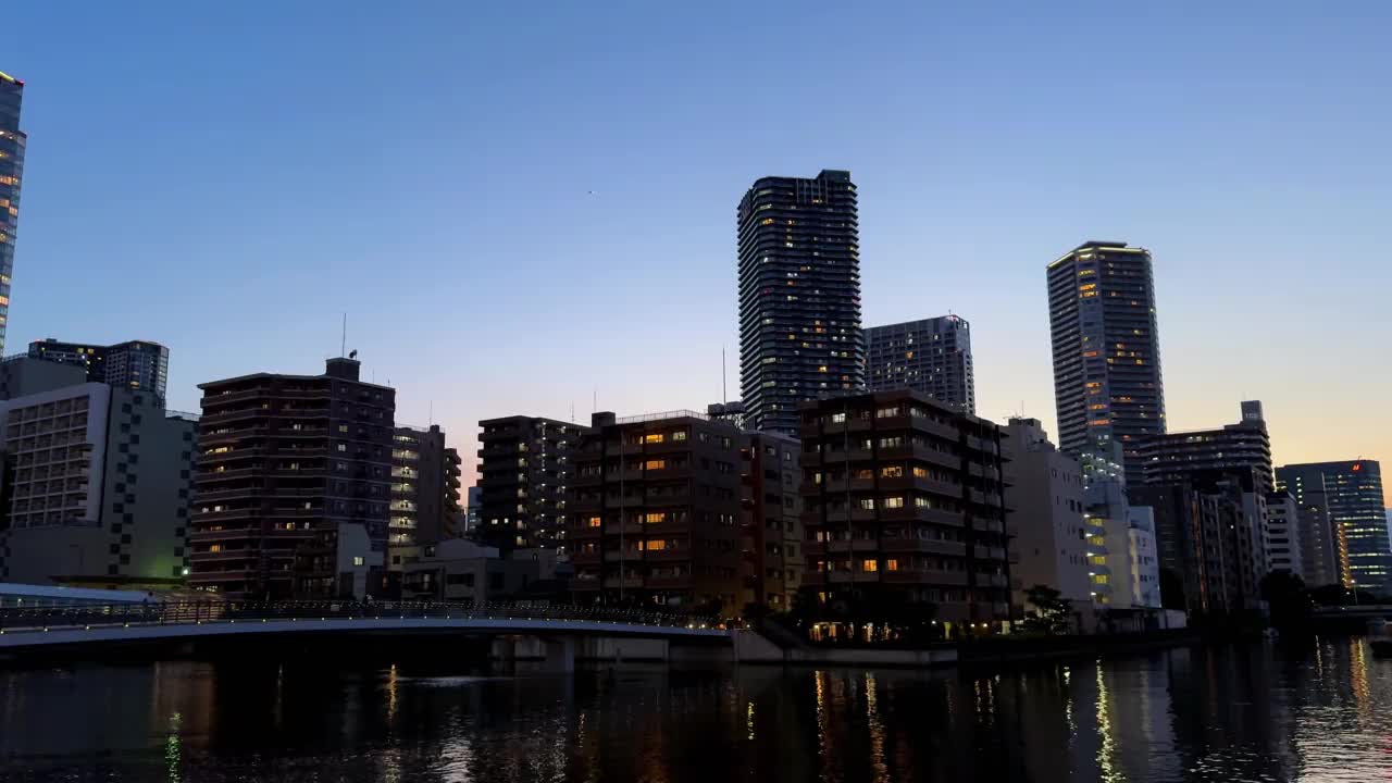 黄昏时分的城市天际线，灯火通明的建筑物映照在平静的河流上视频素材