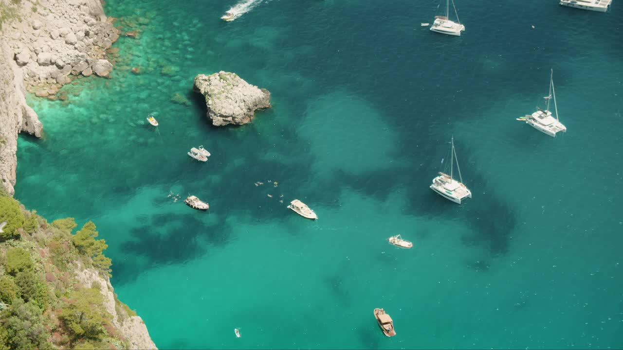 船只漂浮在绿松石般的水面上，靠近意大利卡普里岛的岩石海岸线。在夏季阳光明媚的日子里，游艇上俯瞰大海。视频素材