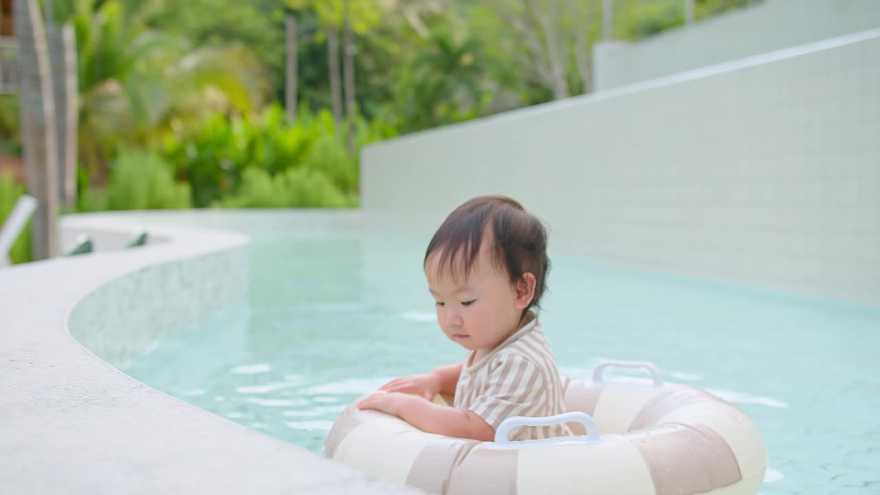 可爱的幼儿女孩戴着太阳镜漂浮在游泳池与充气环在一个现代化的度假胜地周围郁郁葱葱的绿色植物，夏季娱乐和休闲，快乐的童年时刻，户外活动视频素材