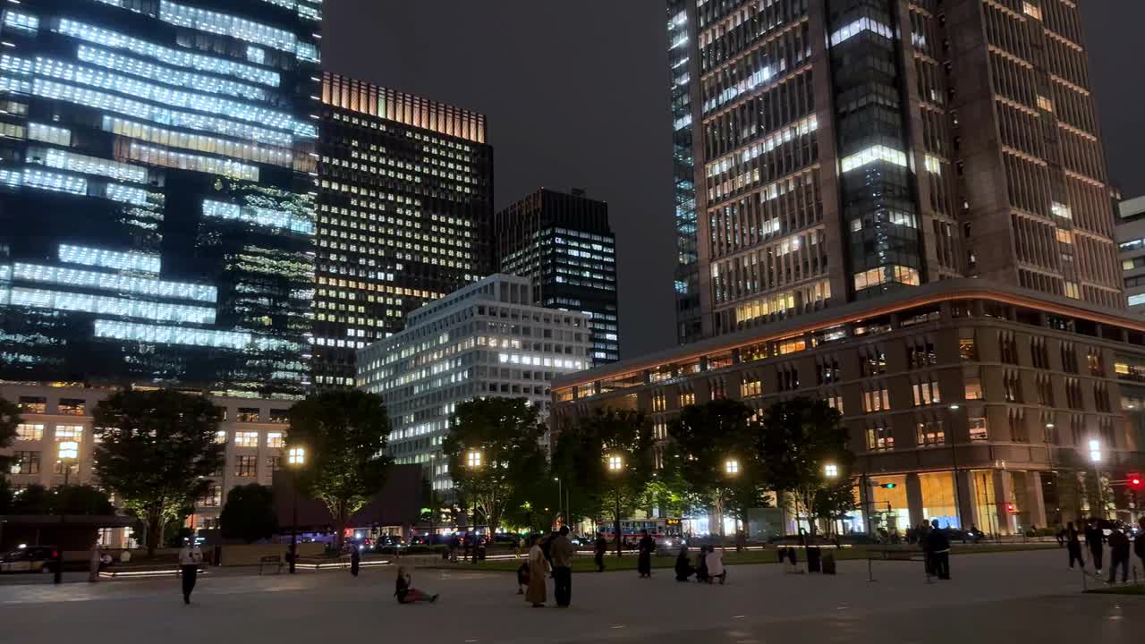 夜晚，人们走在熙熙攘攘的城市广场上，摩天大楼灯火通明视频素材