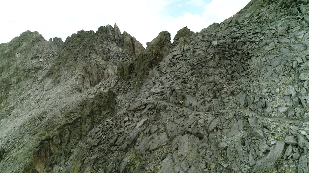 专业登山者在悬崖附近的极端山路上行走的无人机视图。高海拔山地运动的挑战路径。视频素材