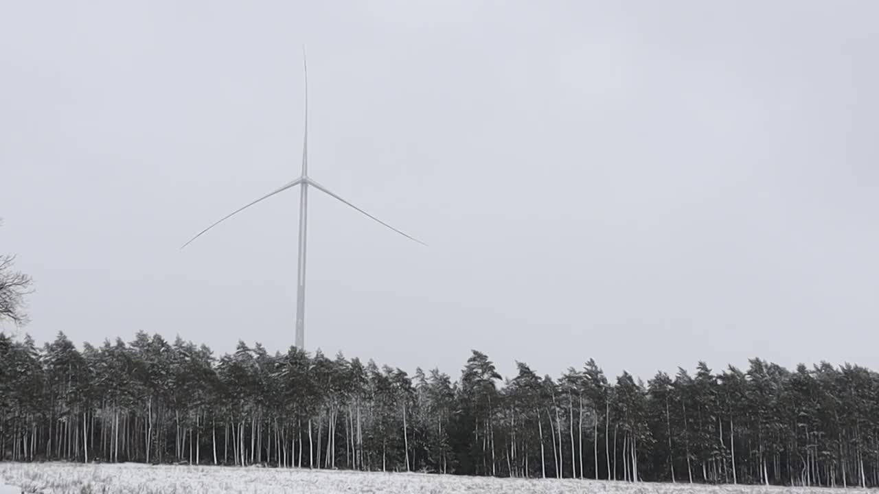 冬天，一个风力涡轮机站在白雪皑皑的森林里，收集可再生能源视频下载