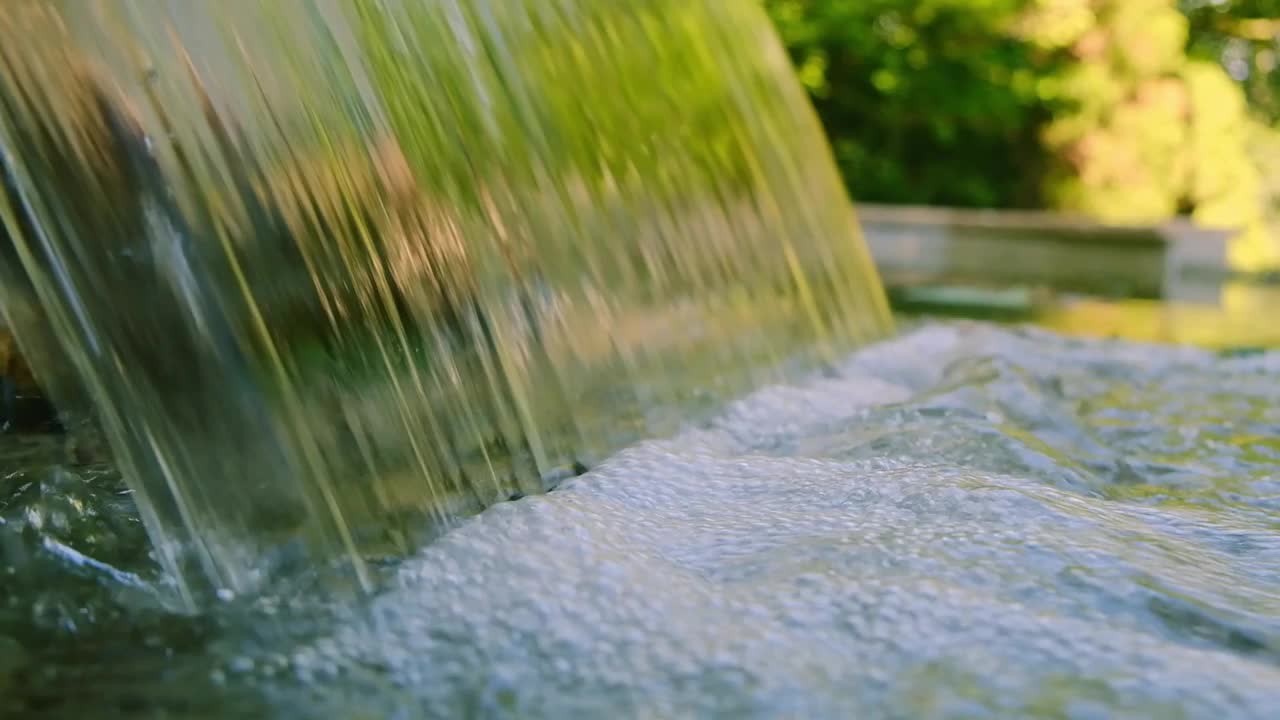 在一个阳光明媚的夏日，一个瀑布倾泻入宁静的水池的特写镜头视频下载