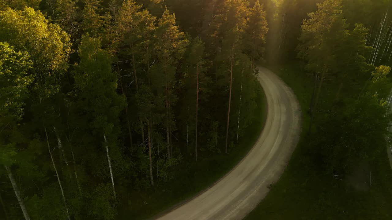 鸟瞰日落时蜿蜒穿过树林的森林道路，捕捉自然景观的宁静之美视频素材